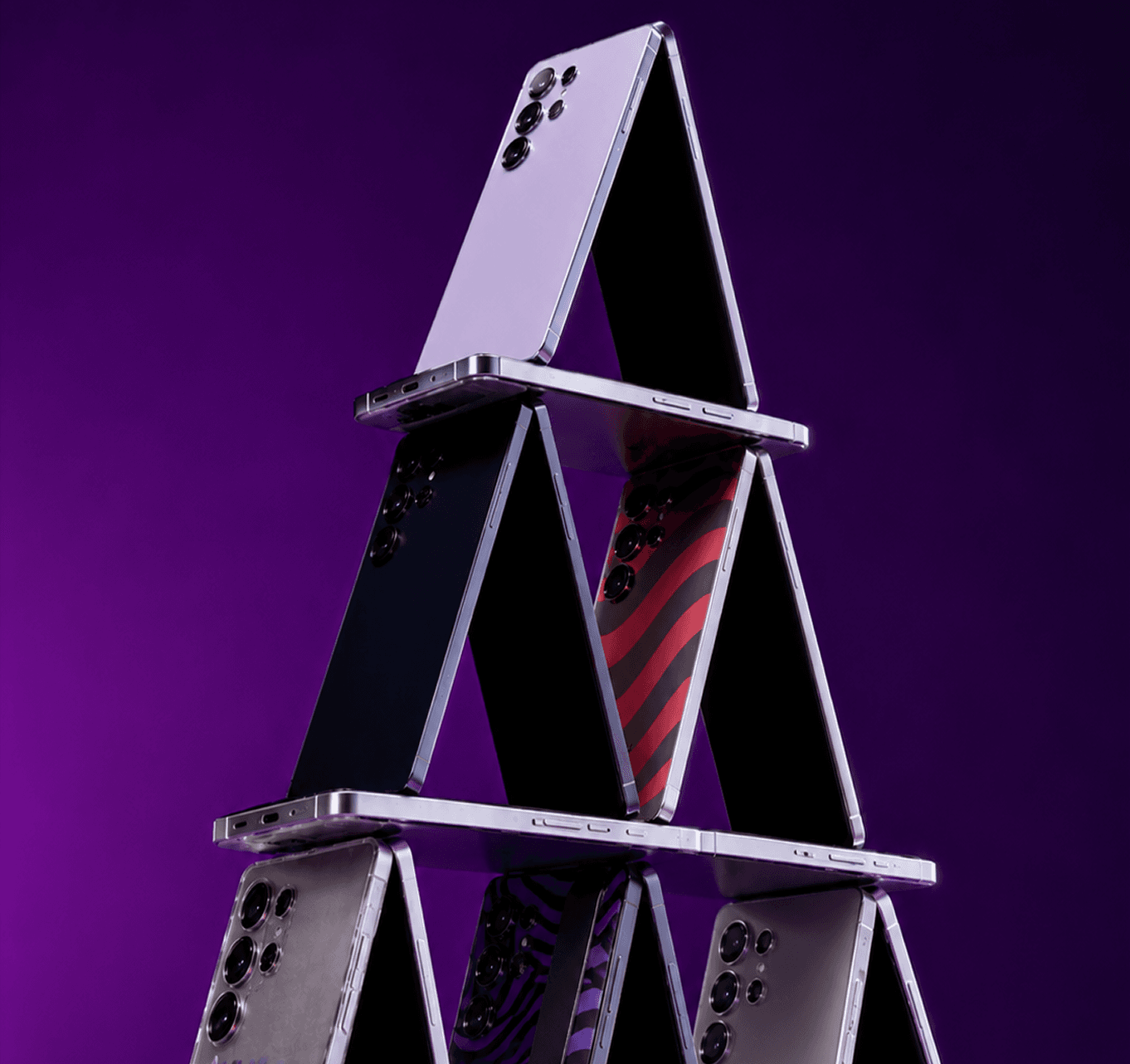 Smartphones balanced into a pyramid against a purple backdrop