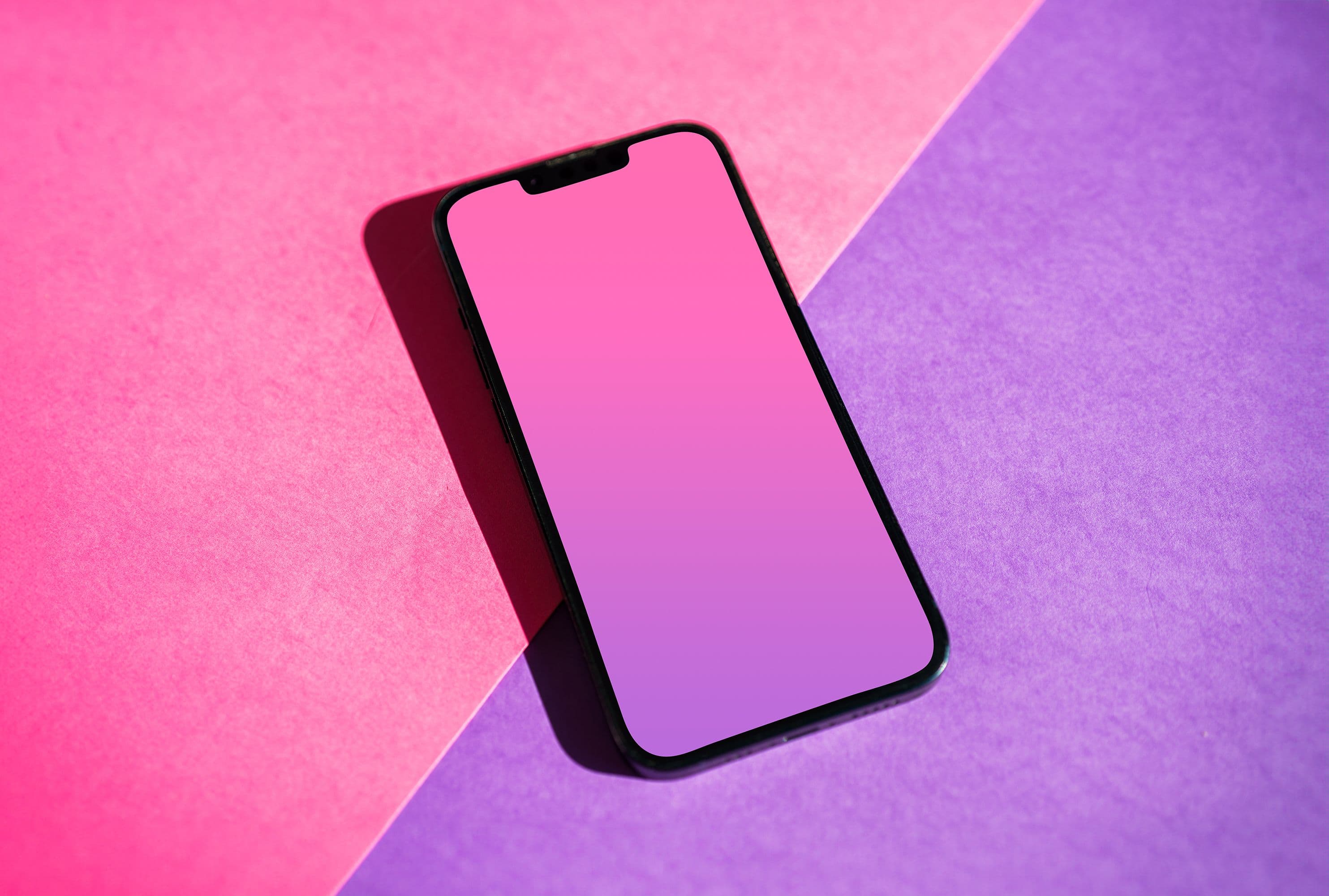A smartphone resting on a pink and purple paper backdrop